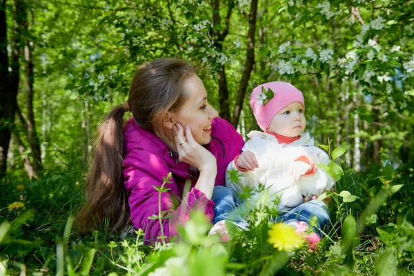 Portrait of young mother and her small daughter in a warm clothes at the park full of apple blossom trees in a spring day. Woman and girl in nature landscape