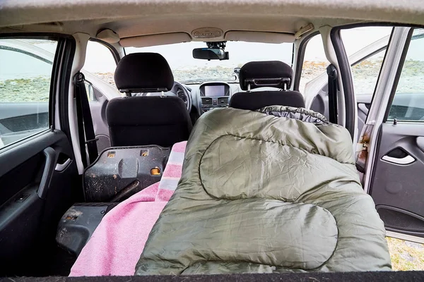 View of a sleeping bag in the cabin of a small car. Overnight in nature near the water of a lake, river, sea or fjord in the cold season. The concept of a trip to nature