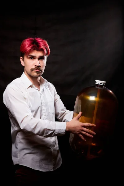 Young handsome guy with red hair in white shirt having fun with beer. Funny man with emotions on face with large bottle of beer and black background. Brewer and barrel. Happy alcoholic with alcohol