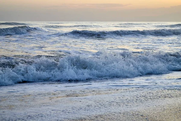 Waves with foam in a water of sea in the evening during sunset