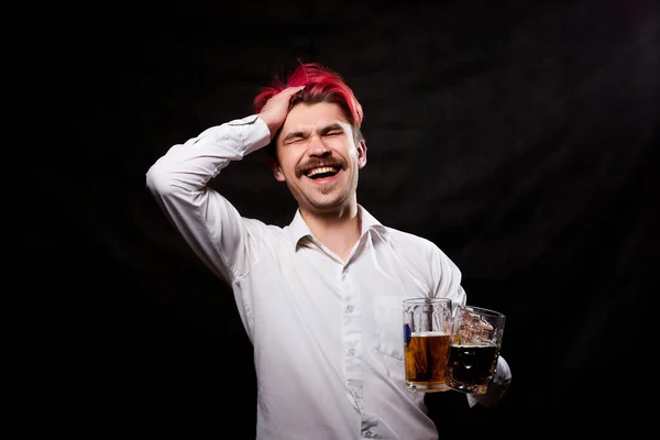 Young handsome guy with red hair in white shirt drinking beer. Funny man with emotions on the face and beer mug in hand and black background. Alcoholic is happy with alcohol. Model in studio