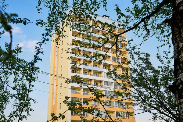 Big house, branch of tree wih green leaves and blue sky with white clouds background. Big block of flats in a summer day in Russia