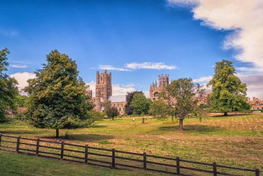 Dağınık bulutlar ve ağaçlarla Ely Katedrali 'nin batı cephesi.