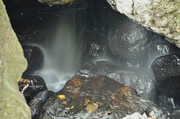 Wasserfall in Höhle hinter Felsen im Wald — Stockfoto