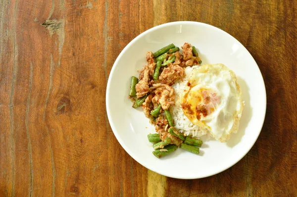 Babi goreng aduk pedas dengan halaman kari kacang panjang topping telur di atas nasi — Stok Foto