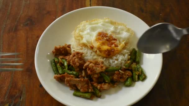 スプーンとフォークで食べる米に長い豆カレートッピング卵を添えた豚肉のスパイシーな炒め物 — ストック動画