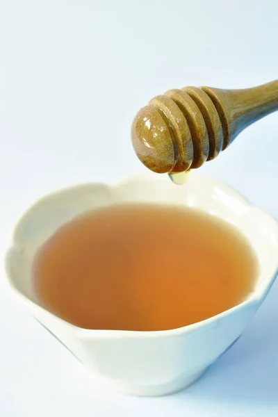 Miel en cucharada de madera gota a taza en fondo blanco — Foto de Stock