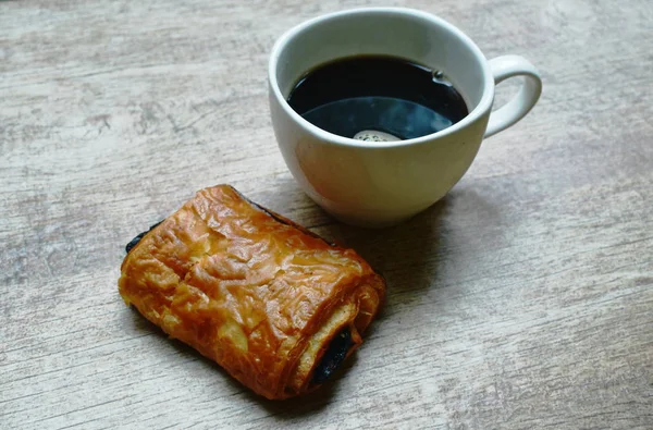 Pan relleno de chocolate y taza de café negro sobre fondo de tabla de madera —  Fotos de Stock