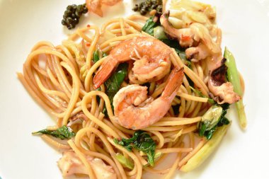  baharatlı tabakta biber ve fesleğen yaprağı ile kızarmış spagetti deniz ürünleri karıştırın