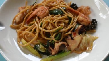 baharatlı biber ve fesleğen yaprağı ile kızarmış spagetti deniz ürünleri karıştırın yemek için gümüş çatal tarafından haddeleme