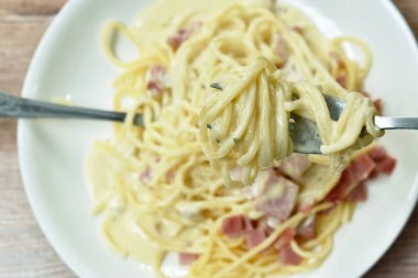 Spagetti beyaz krema sosu dilimlenmiş domuz eti çatal ve kaşıkla servis ediliyor.