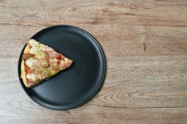 Bir parça pizza sosis ve pastırma ile tabakta peynir.