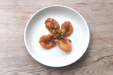 Bol yağda kızartılmış tuzlu nehir karidesi, yanında sarımsak ve tabakta kırmızı biber. 