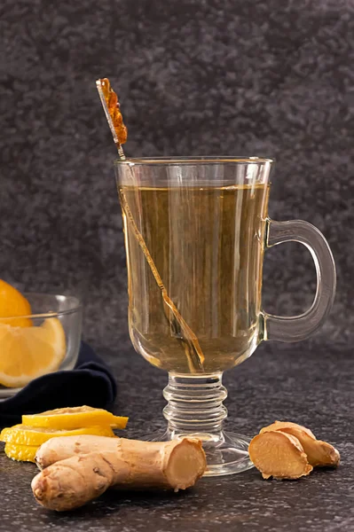 A glass of hot ginger and lemon tea with slices of lemon and ginger root on dark background — Stock Photo, Image