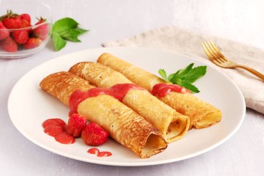 Üç lezzetli krep çilek sosu ve açık gri arka planda bir tabakta çilek. 