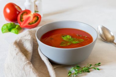 Gri bir kasede domatesli ve açık gri arka planda otlu gazpacho çorbası.