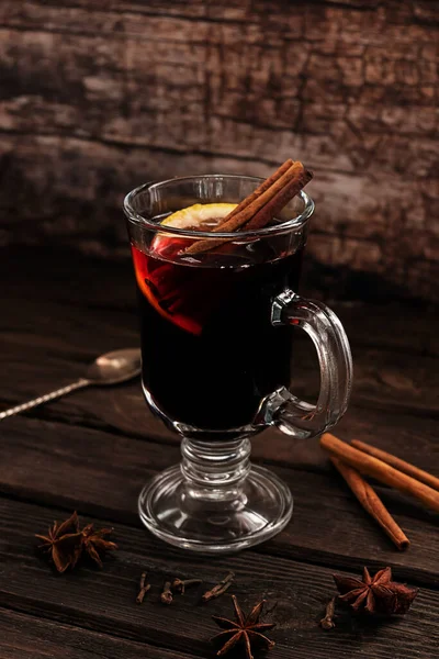 A glass of hot mulled wine with cinnamon sticks and a slice of lemon, on a dark vintage wooden background — Stock Photo, Image