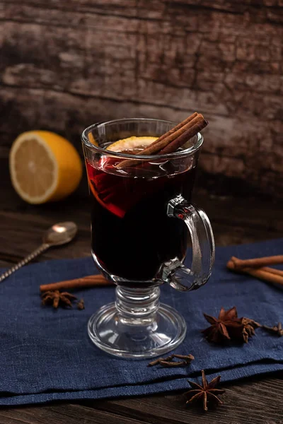 Un verre de vin chaud chaud avec des bâtonnets de cannelle et un citron, avec un textile bleu foncé sur un fond en bois vintage foncé — Photo