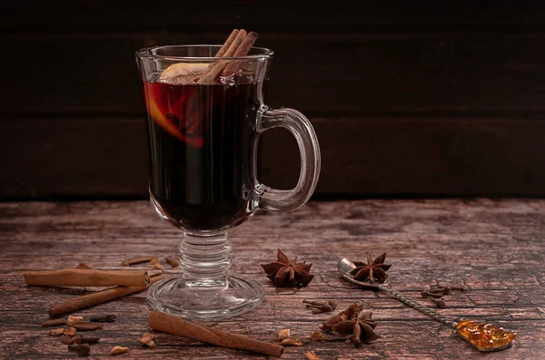 A glass of hot mulled wine with cinnamon sticks and a slice of lemon, on a dark vintage wooden background — Stock Photo, Image