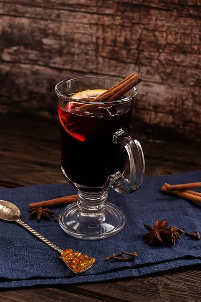 Um copo de vinho quente quente com paus de canela e uma fatia de limão, com tecido azul escuro em um fundo de madeira vintage escuro — Fotografia de Stock