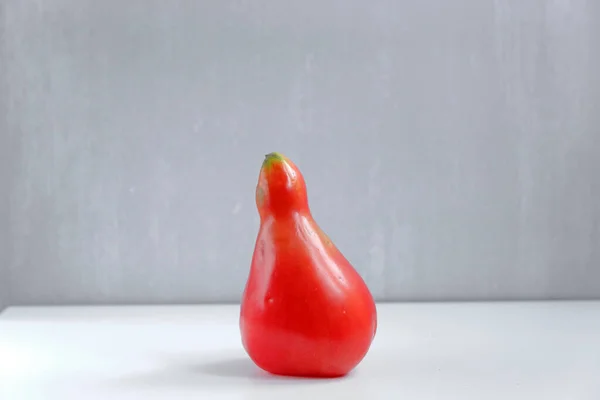 Pear-shaped red tomato on a grey background