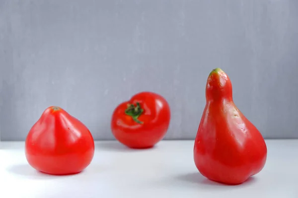 One pear-shaped red tomato and two normal ones on a grey background