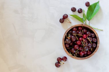 Gri beton arka planda, ahşap bir kasede fotokopi alanı olan taze kirazların üst görüntüsü.