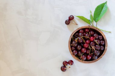 Gri beton arka planda, ahşap bir kasede fotokopi alanı olan taze kirazların üst görüntüsü.