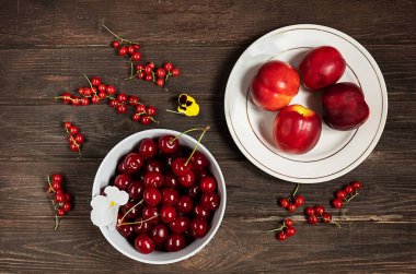 Bir kasedeki kiraz manzarası, beyaz tabakta nektarinler ve eski ahşap arka planda kırmızı frenk üzümü. 