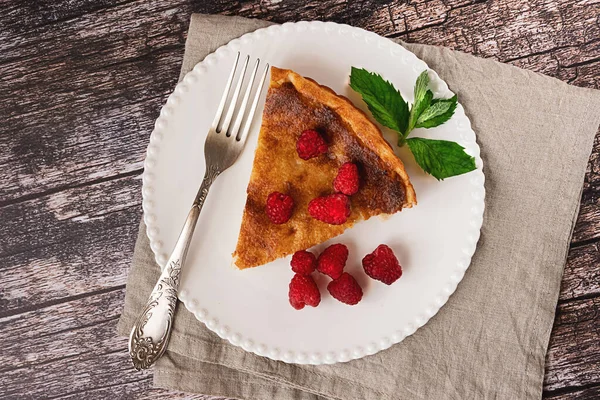 Sweet home-made cheesecake served with raspberries on a white plate on vintage wooden background, flat lay