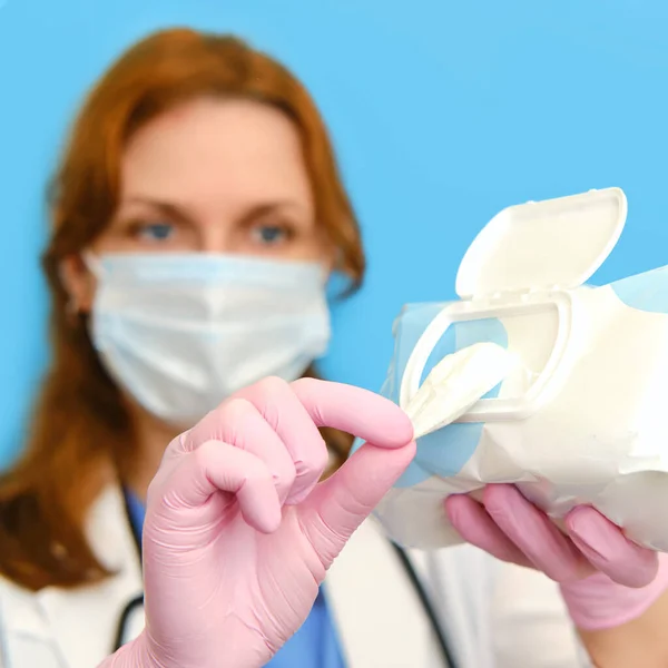 Woman nurse in medical mask with cleaning wipes on a blue background, close-up face.