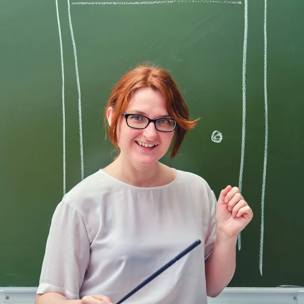 A happy teacher smiles against the background of the school door drawn in chalk