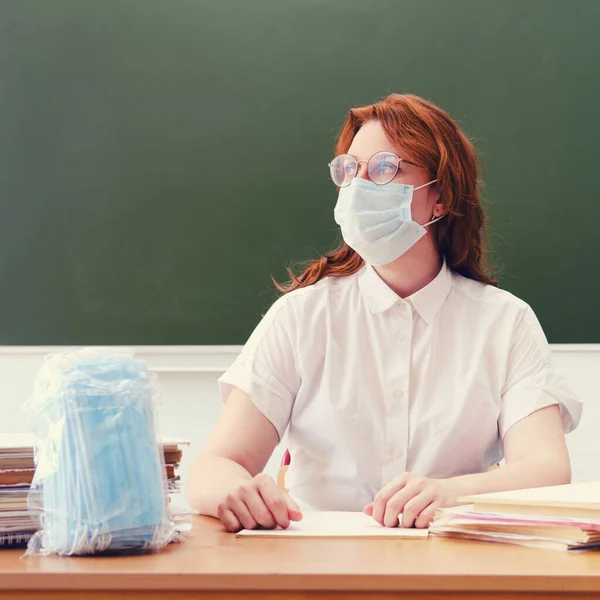 A female teacher in a medical mask is teaching a lesson during the coronavirus epidemic. Problems of education and online learning at school