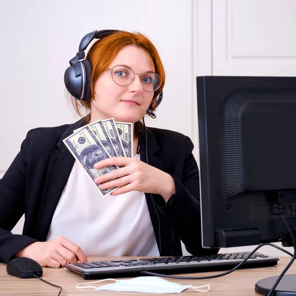 Businesswoman in a suit at a desk with us dollars in hand. Remote work via the Internet during coronavirus quarantine. Business woman at the computer monitor in the home office
