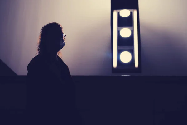 Silhouette of a woman in a medical mask and a lamp