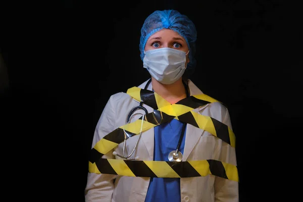 Tied with a warning tape, a nurse in a medical uniform on a black background. The concept of doctors defenselessness work of a coronavirus epidemic