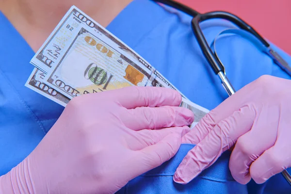 The doctor hides the us dollar bills in the pocket of the medical uniform. A nurse with money to buy medicine for coronavirus
