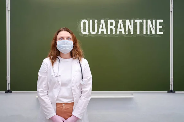 Sad school doctor in a face mask at the blackboard. The text Quarantine is written in chalk