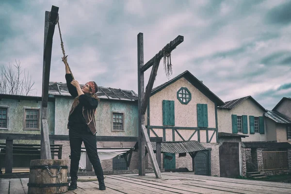 A pirate girl cuts the rope of the gallows with a cutlass in the square of the old city