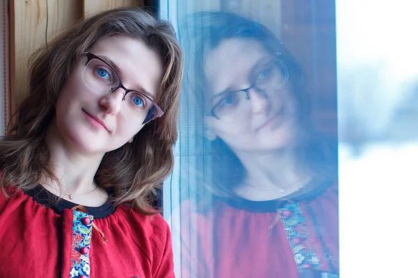 A woman in folk clothes stands next to the winter window