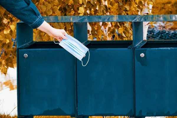 Hand throws a protective mask into a garbage can, closeup