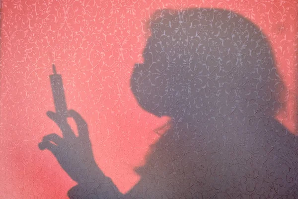 Shadow of a woman silhouette on a syringe for injection. Protection against covid-19 coronavirus infection. Silhouette of a doctor who looks at a patient with the flu virus in quarantine