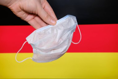 Hand holding a mask on the background of the German flag. To combat coronavirus in the German cities
