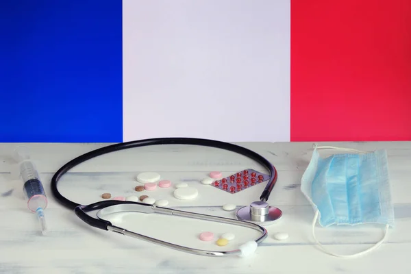 French flag on the background of pills, stethoscope and medical mask on the table. The flag of France and medical supplies