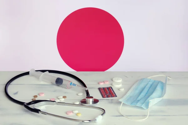 Japanese flag on the background of tablets, stethoscope and medical mask on the table. The flag of Japan and medical supplies