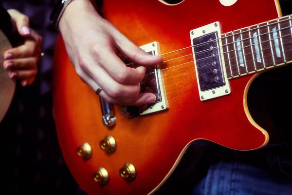 A man hand on the strings of a red guitar. Long fingers play the electric guitar in the recording Studio. Life style from the recording of the song at the recording Studio.