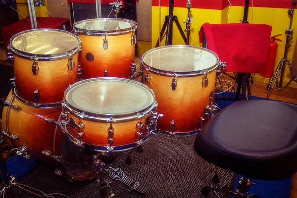 Orange drums and a black chair in the rehearsal room. Yellow and red walls in the room for musicians.