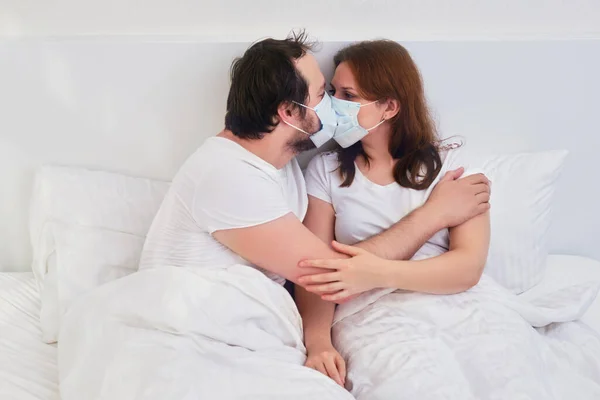Couple kissing in bed in medical mask. Family relationships in isolation due to coronavirus.