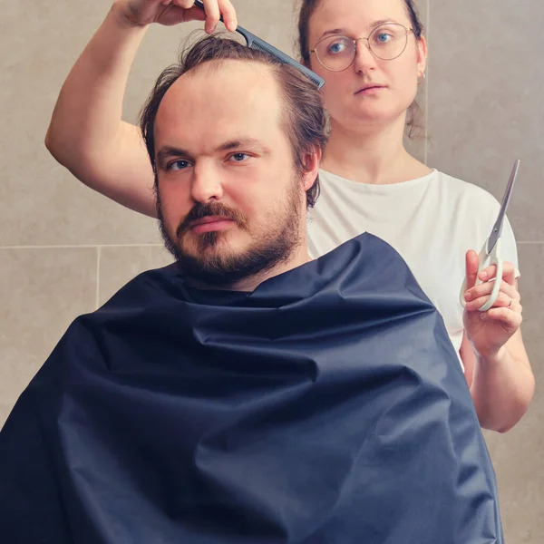 A woman cuts a man\'s hair at home in the bathroom, lifestyle. Concept of self-cutting and shaving during the flu epidemic