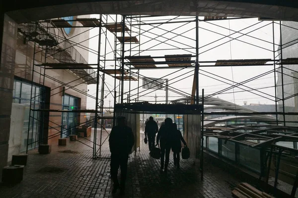 Scaffolding in the pedestrian area. People go next to the building under construction. Silhouettes of people on the background of construction.